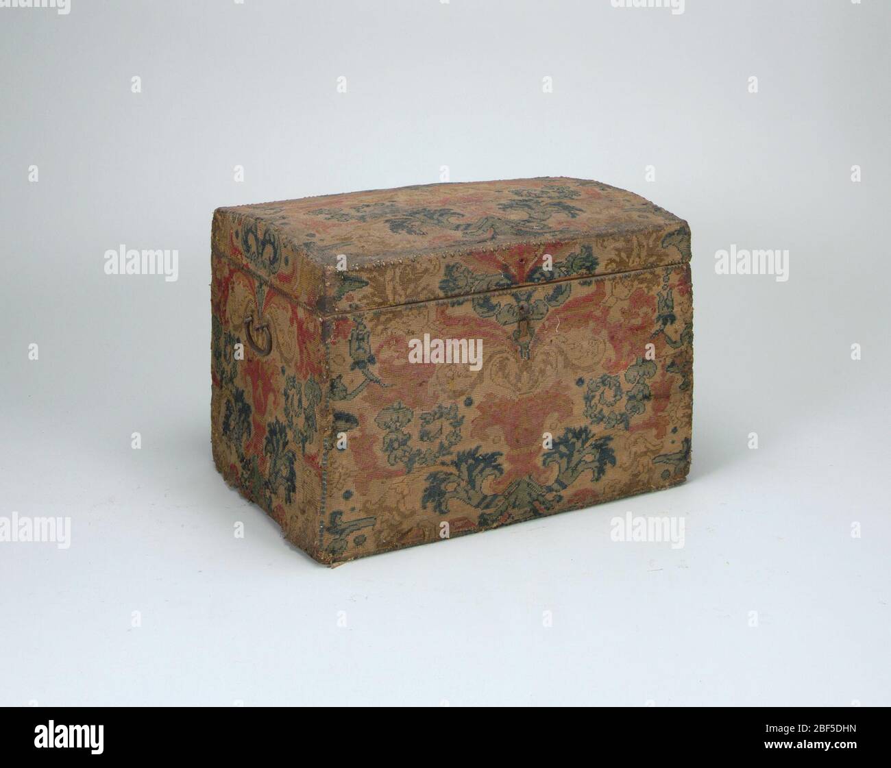 Trunk. Tronco con coperchio a cupola, dotato di piastre angolari in ferro e maniglie, bordi con chiodi in ottone. Ricoperto di ago in lana con audace chiocciola e disegno floreale lavorato in punto tenda, nei toni del rosso, giallo e blu. Coperchio danneggiato e usurato. Foto Stock