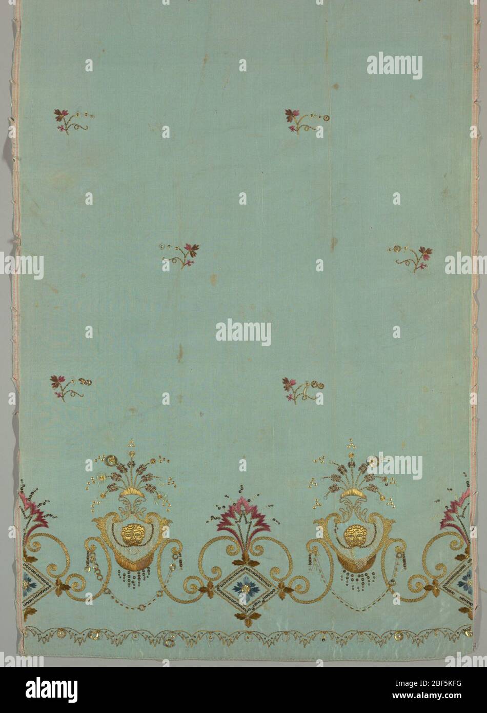 Pannello. Il pannello di seta azzurro, destinato ad una gonna, ha un bordo ricamato in seta colorata, filo metallico e paillettes, e un applé di rete bianca. Disegno di curve a S invertite che sorreggono un telaio a forma di cuore con una maschera di leone al centro. Foto Stock