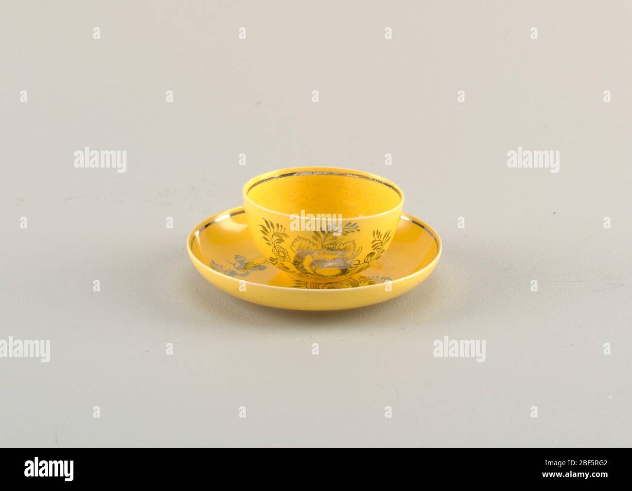 Tazza e piattino. Coppa gialla e piattino con bordi capovolto. Entrambi decorati con motivi floreali metallici e fascia intorno ai bordi. Foto Stock