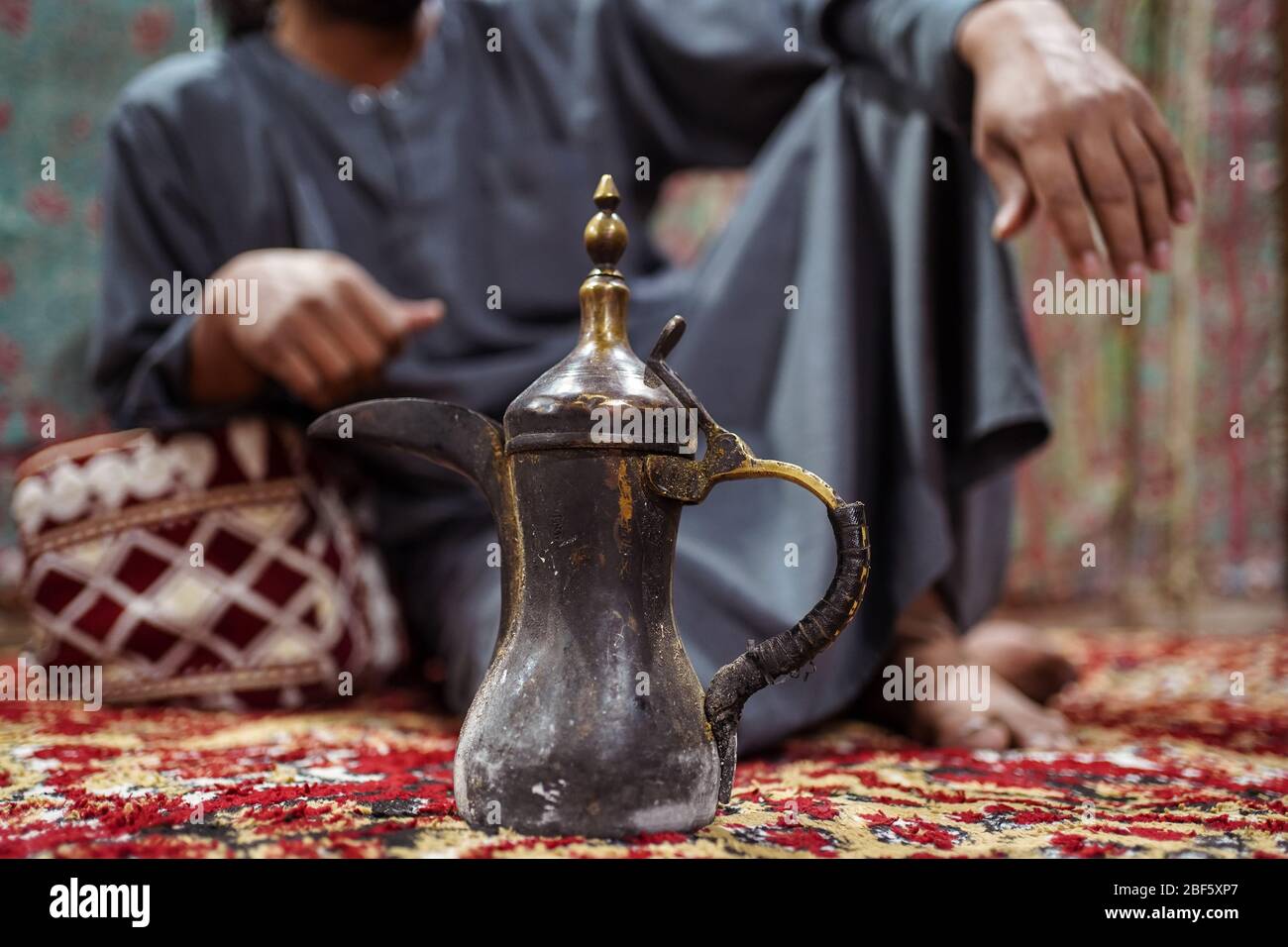 Primo piano della tradizionale teiera araba con l'uomo beduino che indossa abiti tradizionali seduti su un tappeto nel deserto Saudita, Arabia Saudita Foto Stock