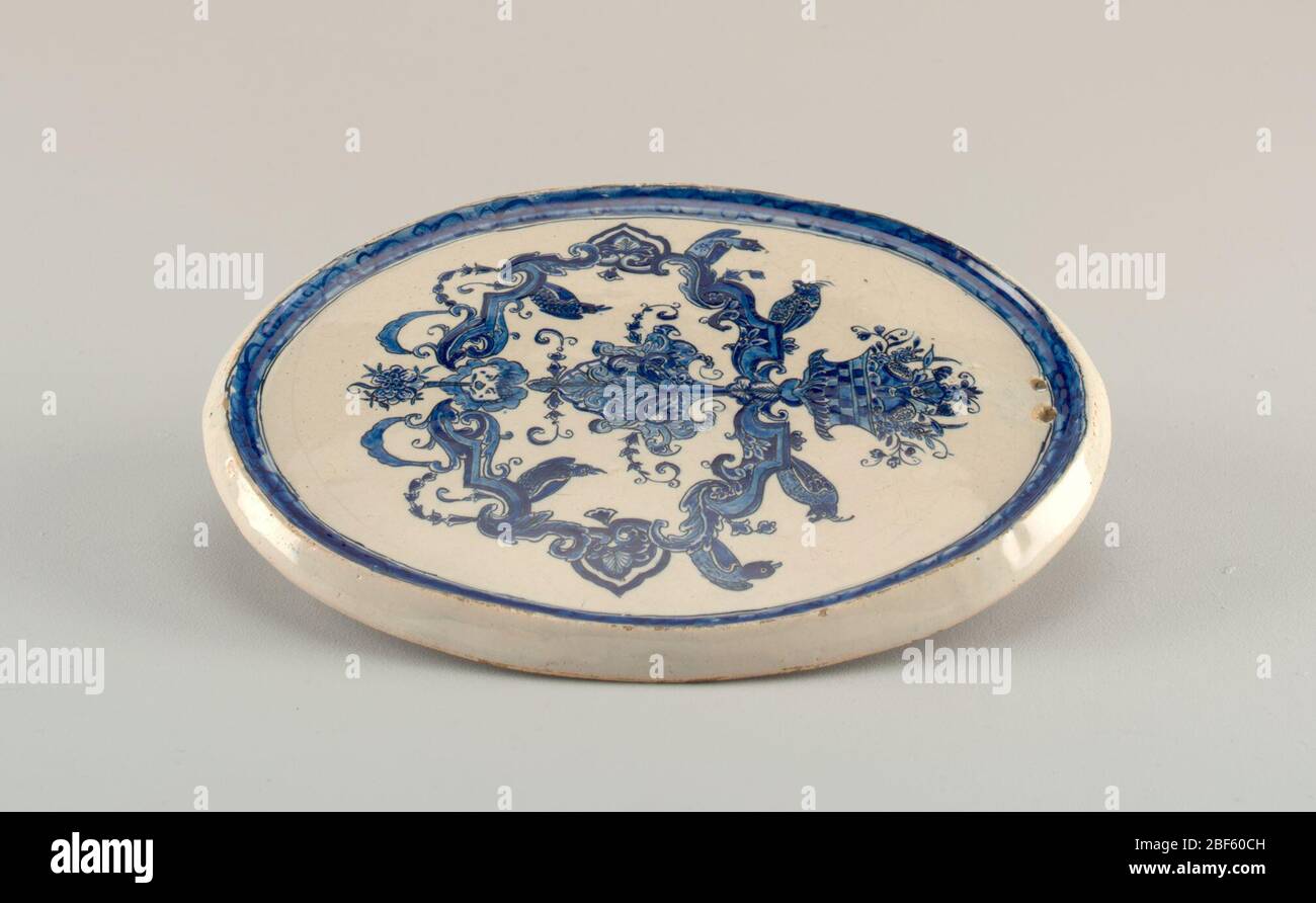 Placca. Placca ovale con bordo sagomato, 2 fori in alto per appendere; dipinta in blu opaco su bianco con decorazione grottesca composta da frutta, uccelli, maschera, lambrequin; intorno al bordo con un motivo a chiocciola ricoperto di blu; fondo liscio. Foto Stock