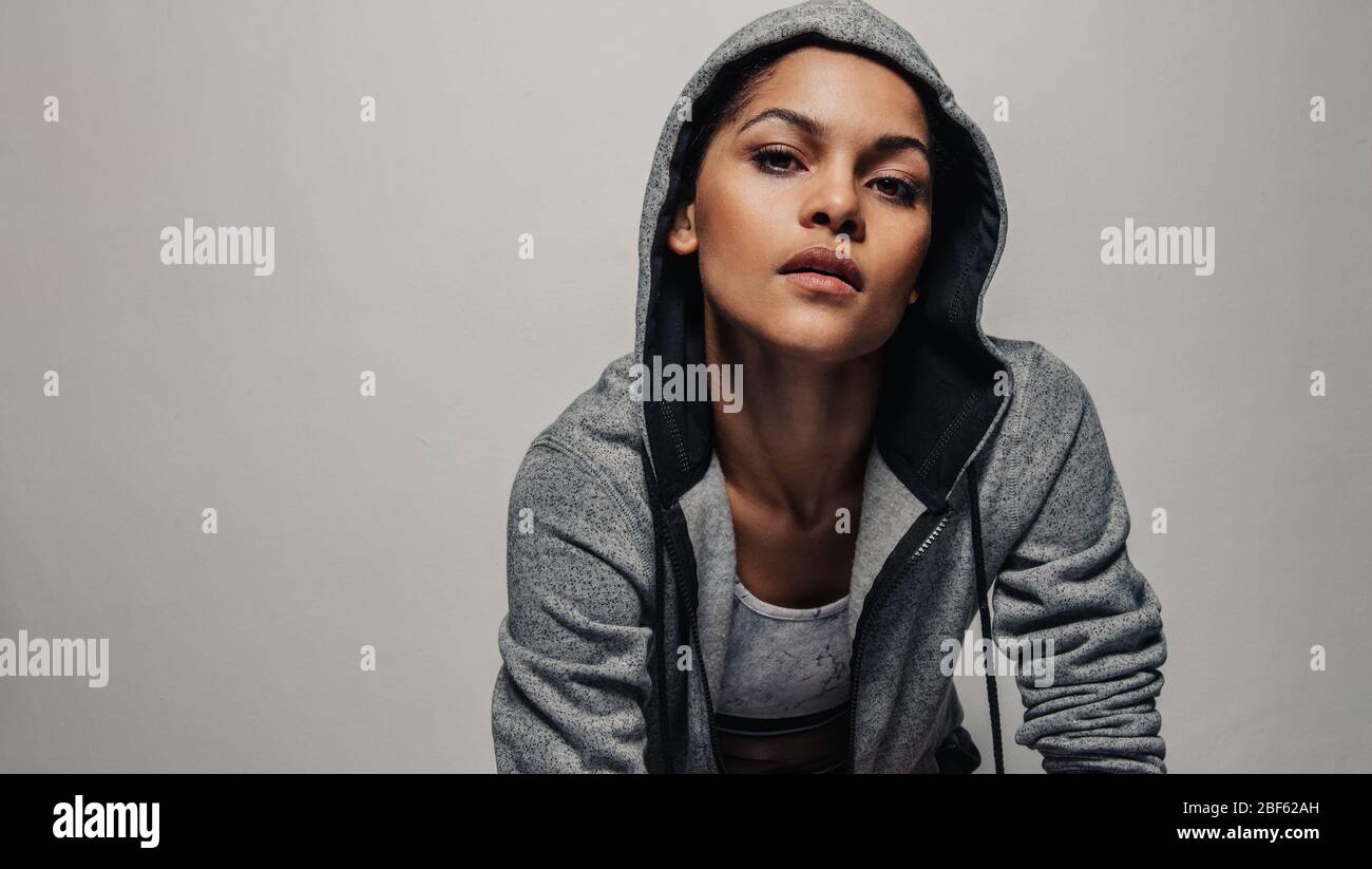 donna in forma fisica che indossa una giacca con cappuccio che fissa la fotocamera. Donna sana in abbigliamento sportivo su sfondo grigio. Foto Stock