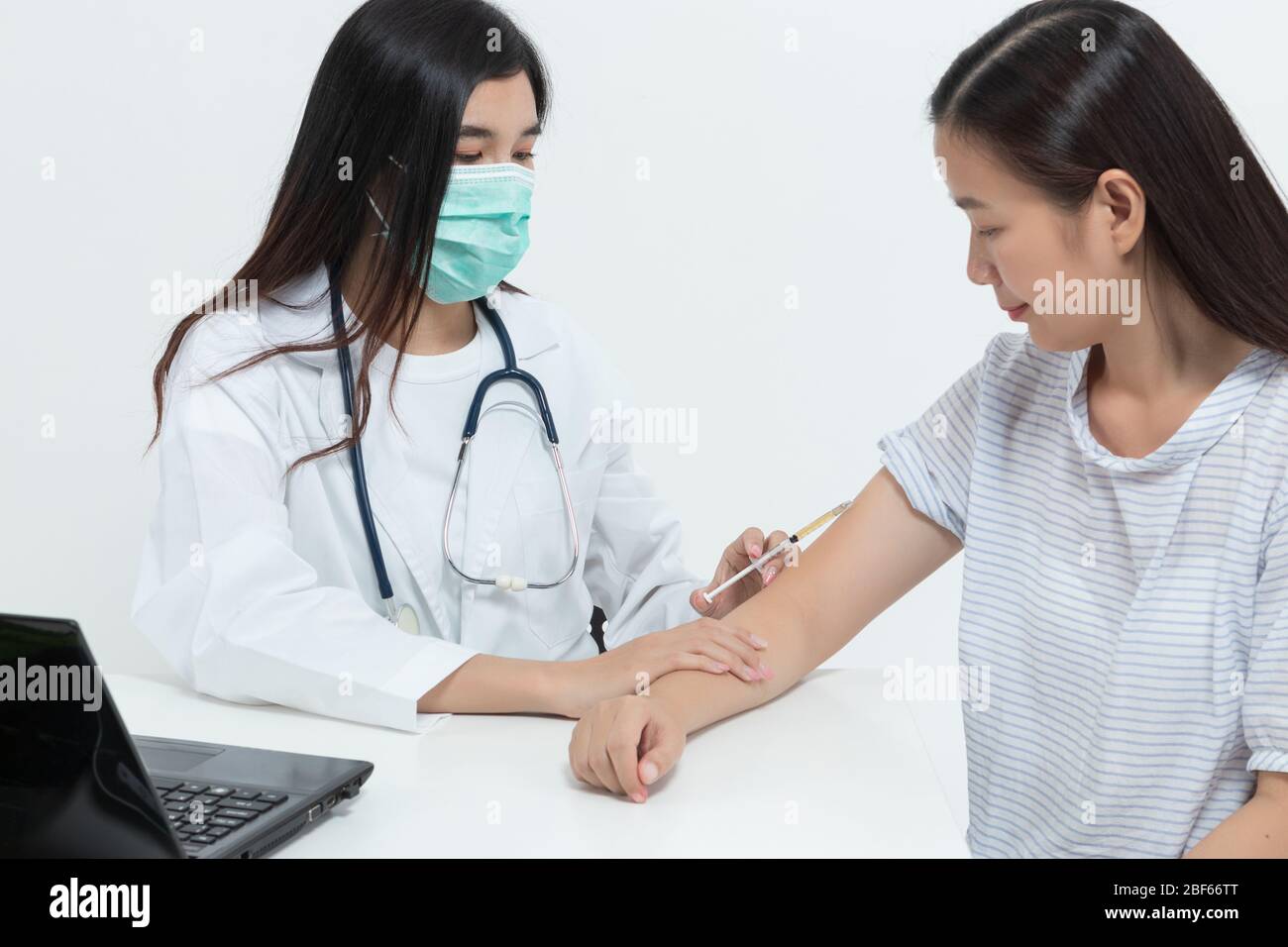 Giovane donna medica asiatica che indossa maschera medica e stetoscopio sta esaminando il paziente e trattandola iniettando la medicina in clinica o ospedale. H Foto Stock