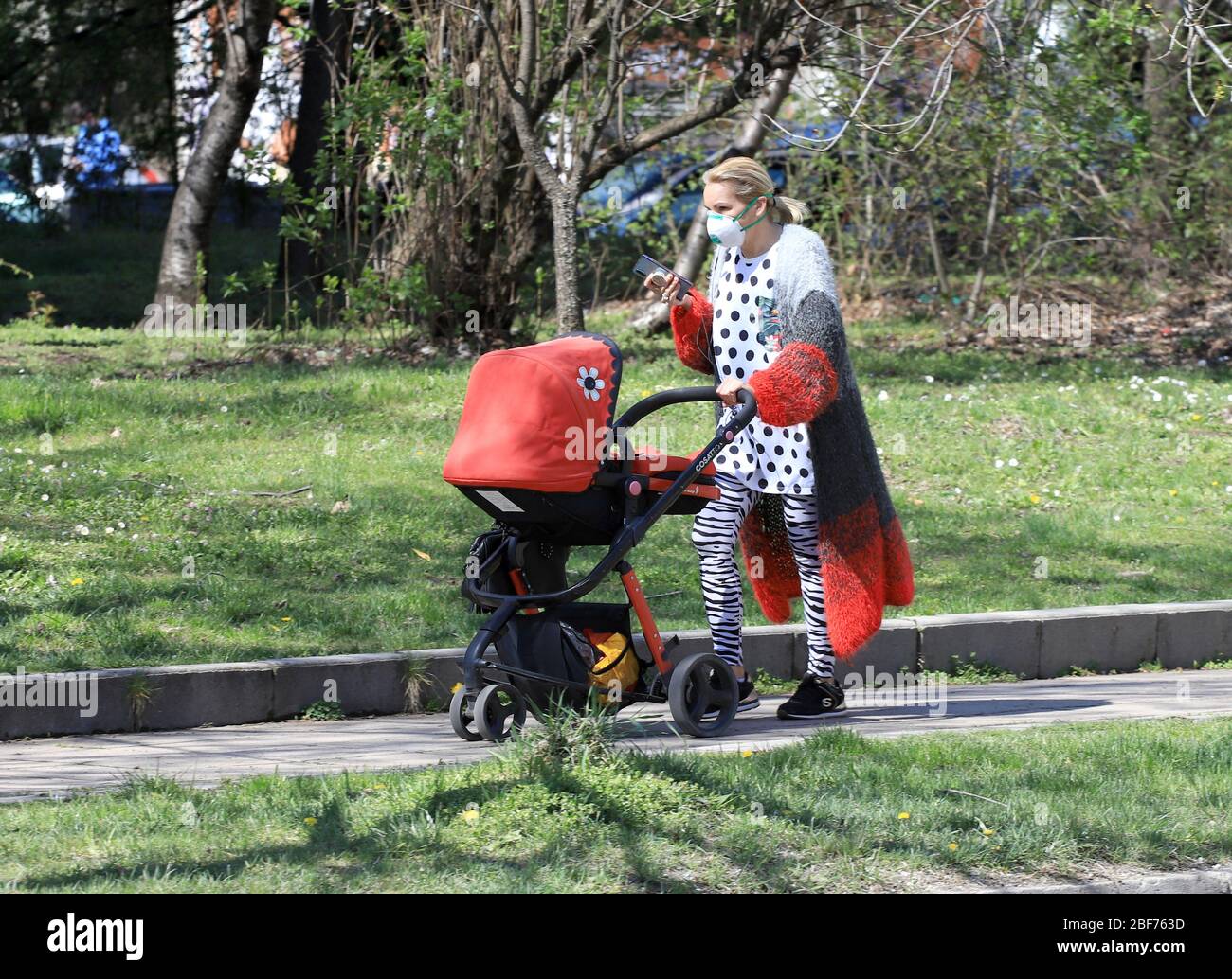 Donna con maschera facciale per la protezione da coronavirus spingere un passeggino in strada a Sofia, Bulgaria il 04/16/2020 Foto Stock