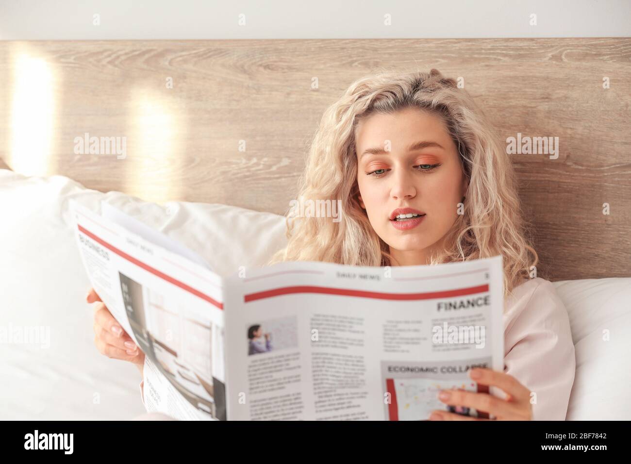 Mattina di bella giovane donna lettura giornale a letto Foto Stock