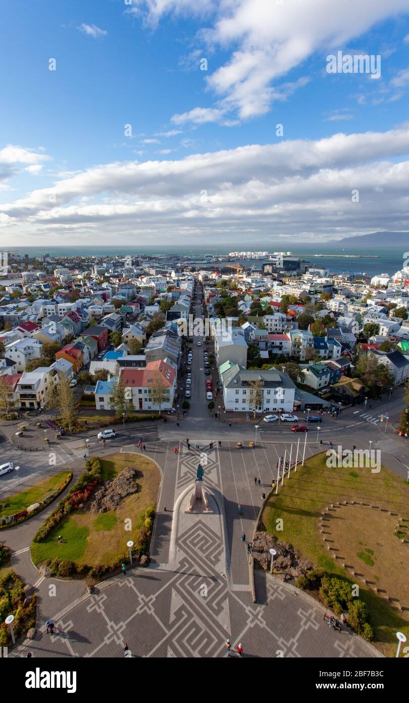 Vista dalla chiesa di Hallgrímskirkja, Reykjavík in Islanda, che mostra case colorate, un cielo blu con nuvole bianche e grigie e il porto Foto Stock