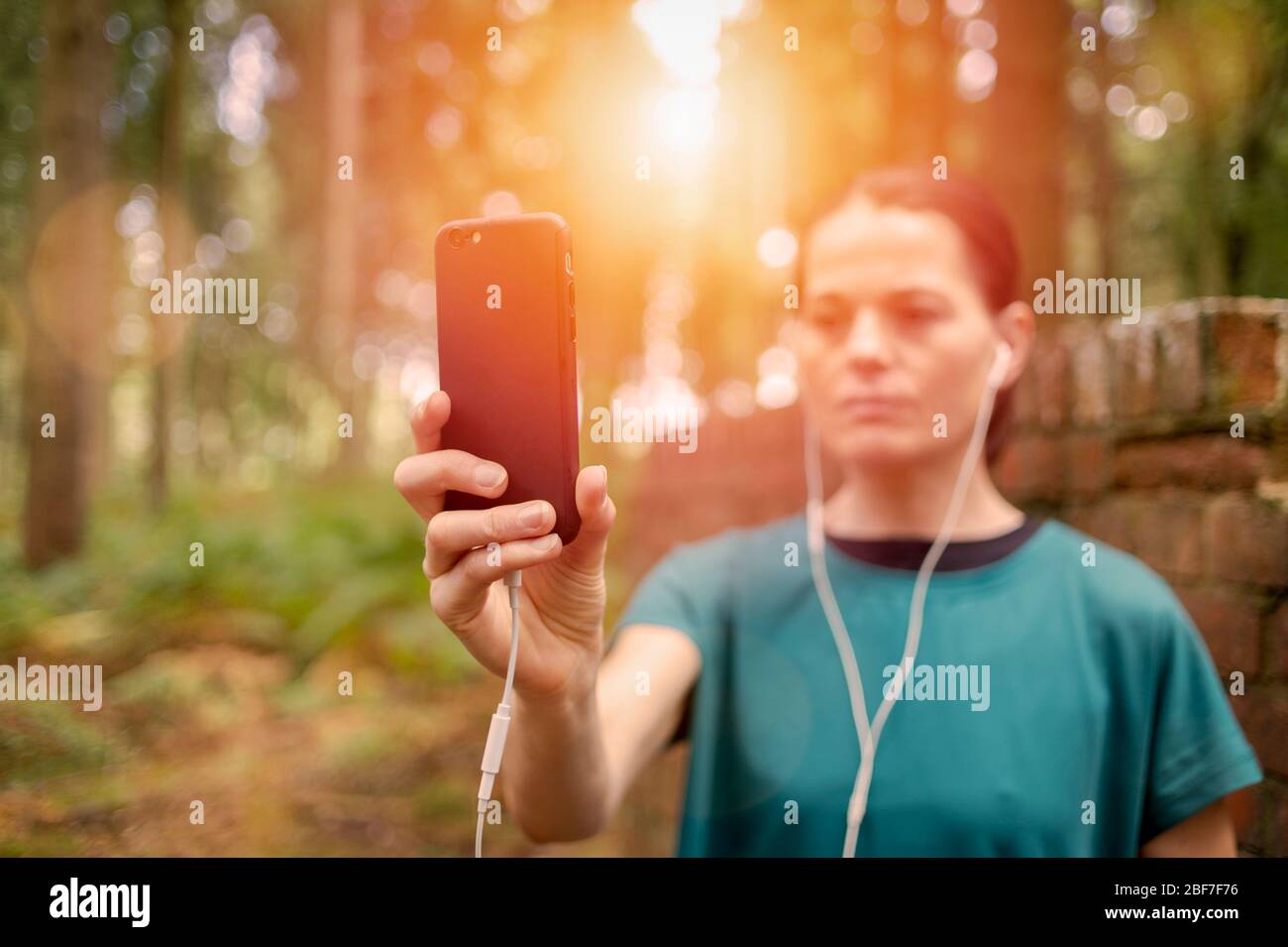 Donna che tiene uno smartphone, ascoltando musica mentre si fa jogging nella foresta Foto Stock
