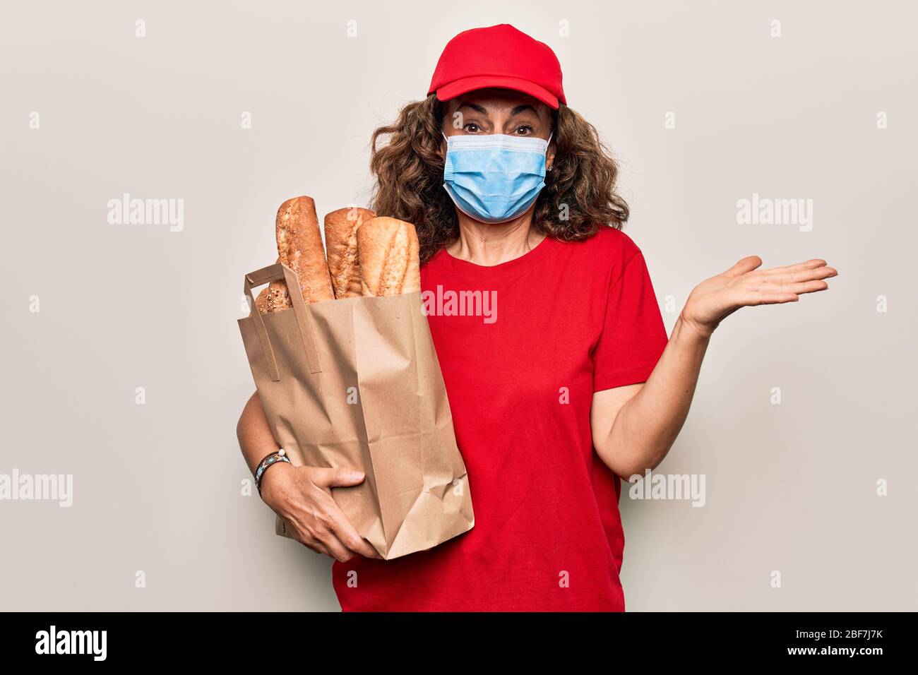 Media età consegna donna che indossa la maschera di protezione coronavirus tenendo take away pane borsa celebrare il successo con sorriso felice e vincitore expressi Foto Stock