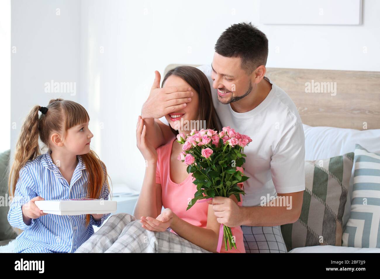 Marito e bambina salutano la donna per la festa della mamma in camera da letto Foto Stock