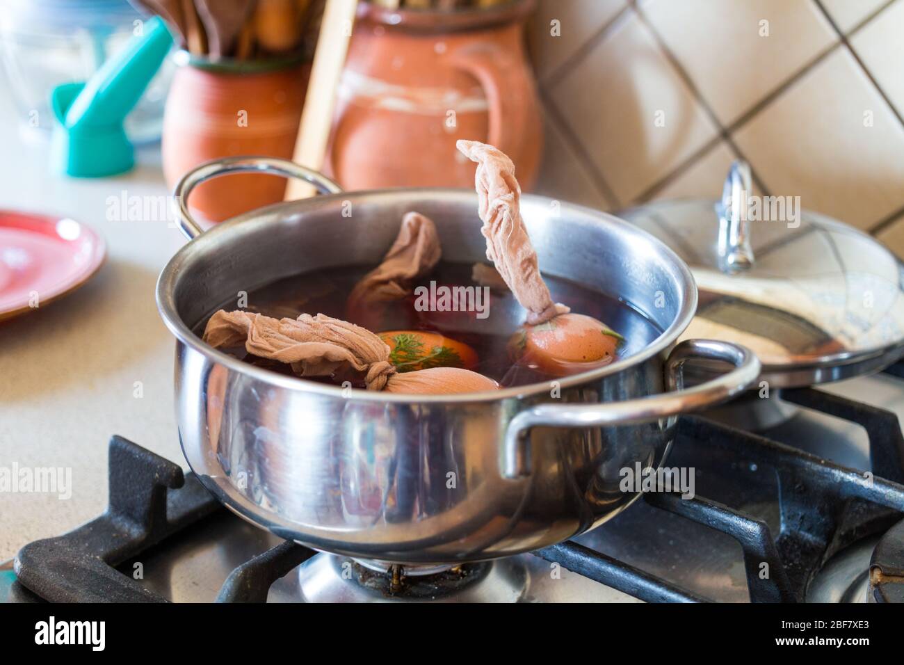Metodo tradizionale di tintura delle uova di pasqua. Piccole foglie di piante pressate sulle uova con calze, mettere in acqua bollente con cipolla rossa. Fase 2 di 3. Foto Stock
