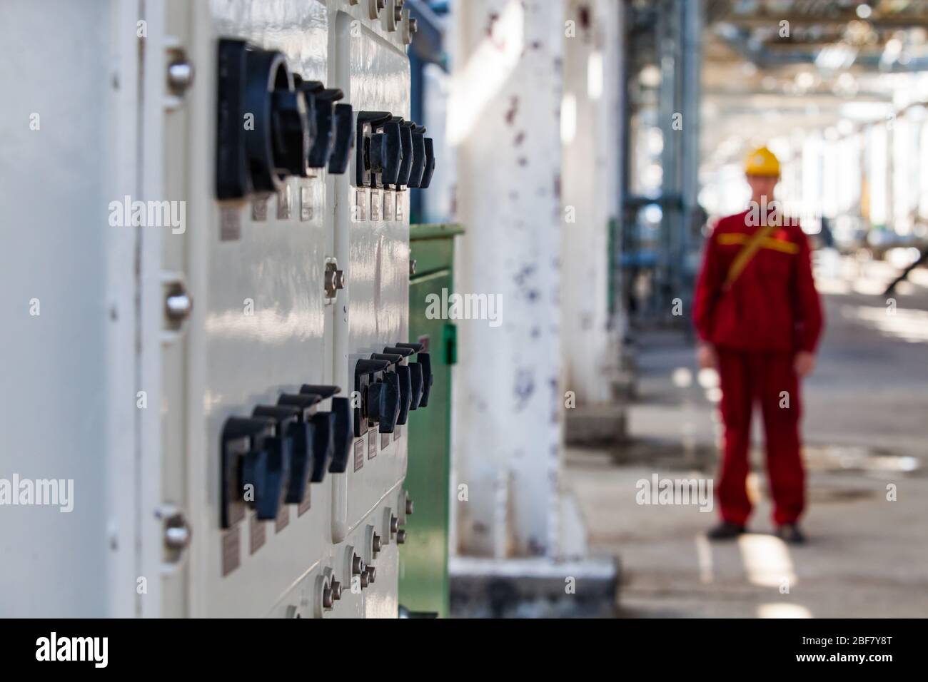 Scheda switcher elettrici. Mettere a fuoco in primo piano. Operaio in rosso lavoro usura e giallo duro aveva offuscato. Impianto di raffineria di petrolio petrolchimico. Società CNPC. Foto Stock