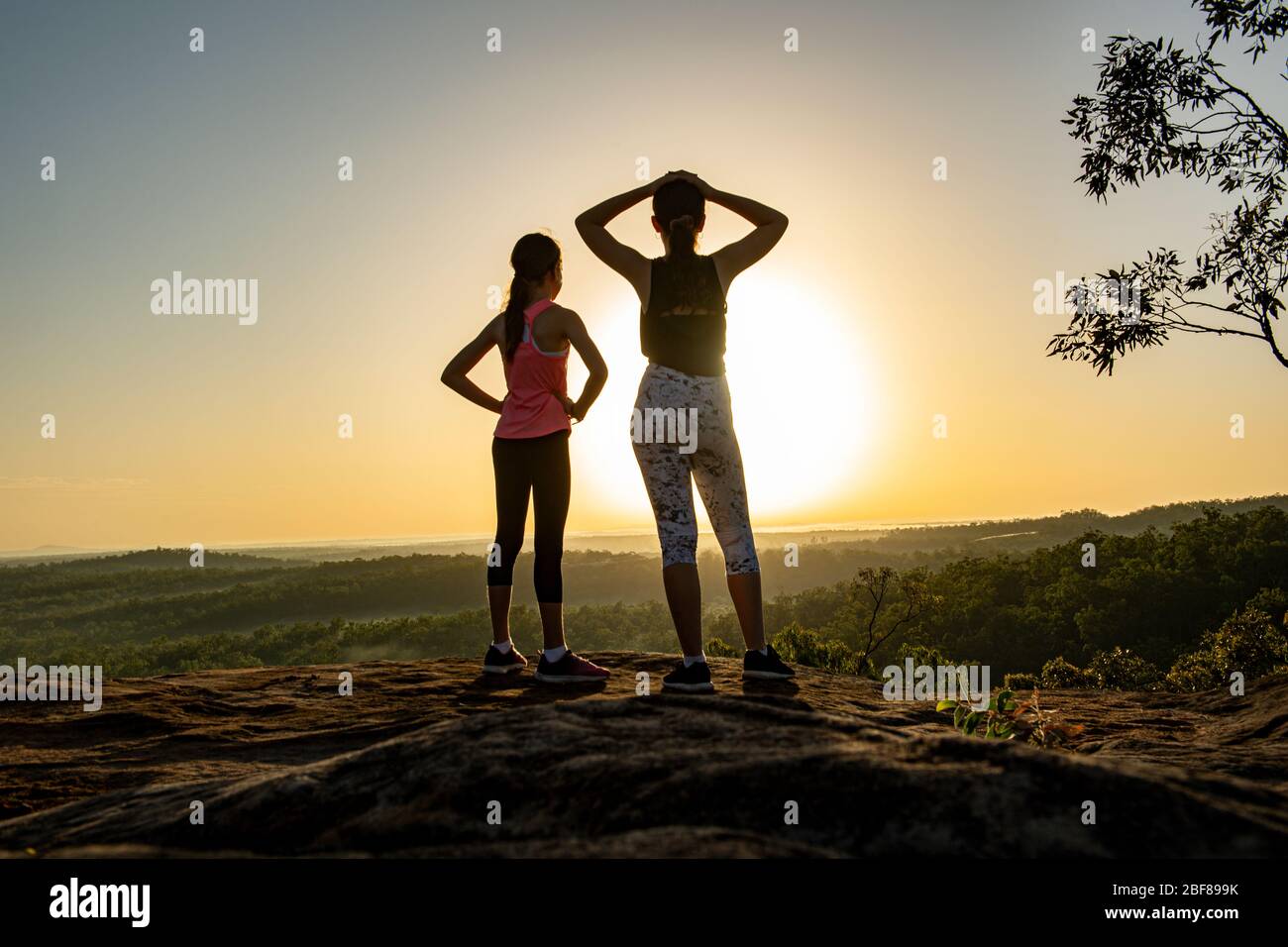 Due giovani donne che si ergono in cima ad una montagna all'alba. Foto Stock