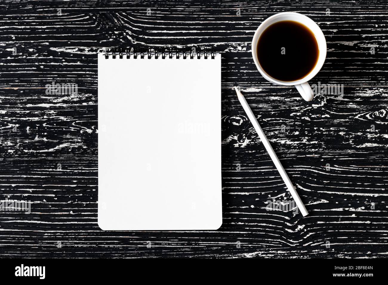Notebook, matite e tazza di caffè su un tavolo di legno nero. Sfondo astratto per il design. Creare una stampa stilizzata o creare un'immonda con spazio per la copia di un testo. Foto Stock