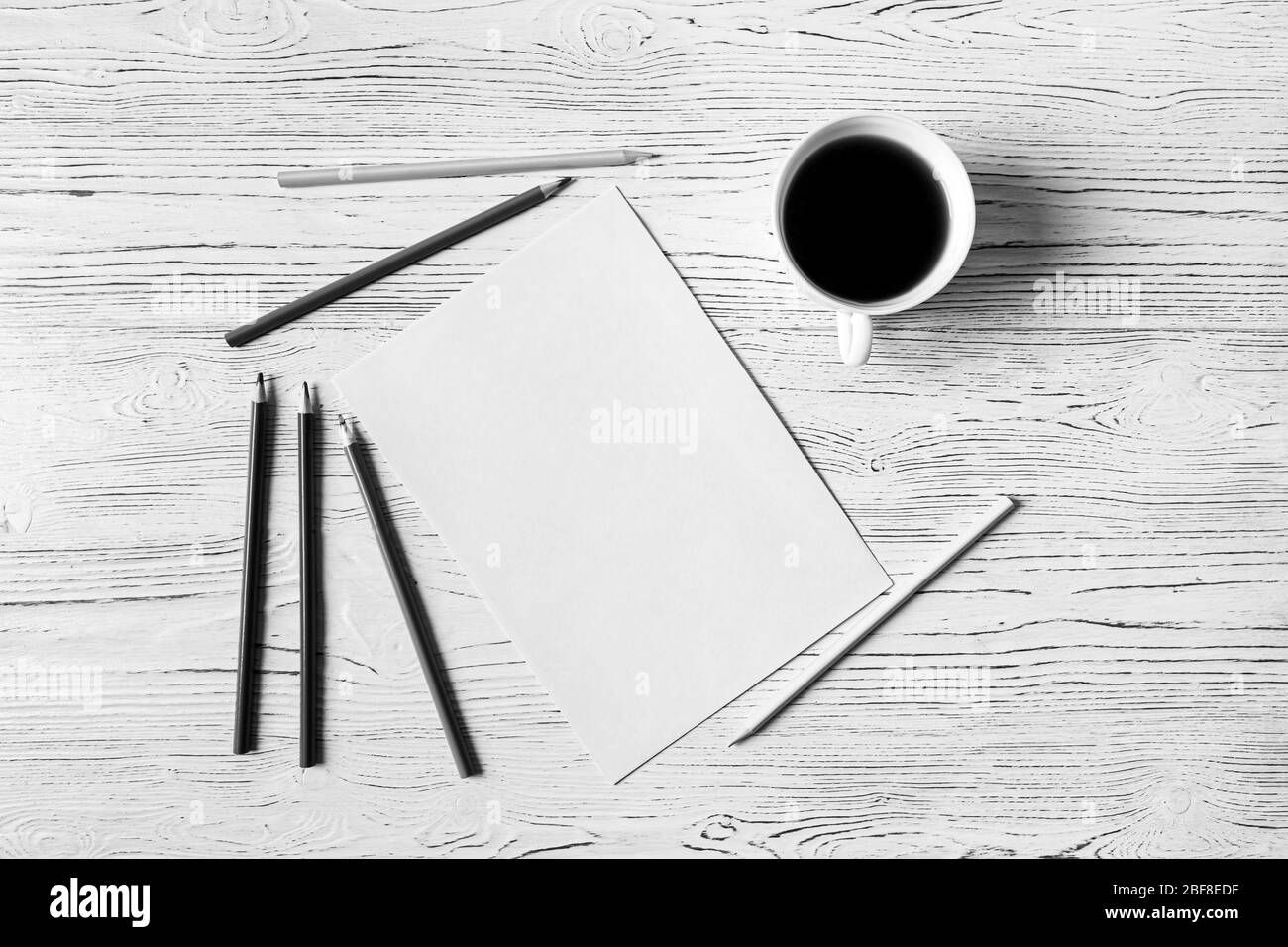 Foglio di carta bianca, matite e tazza di caffè su un tavolo di legno. Sfondo astratto per il design. Art stilizzato baner o mock up con spazio di copia per una te Foto Stock