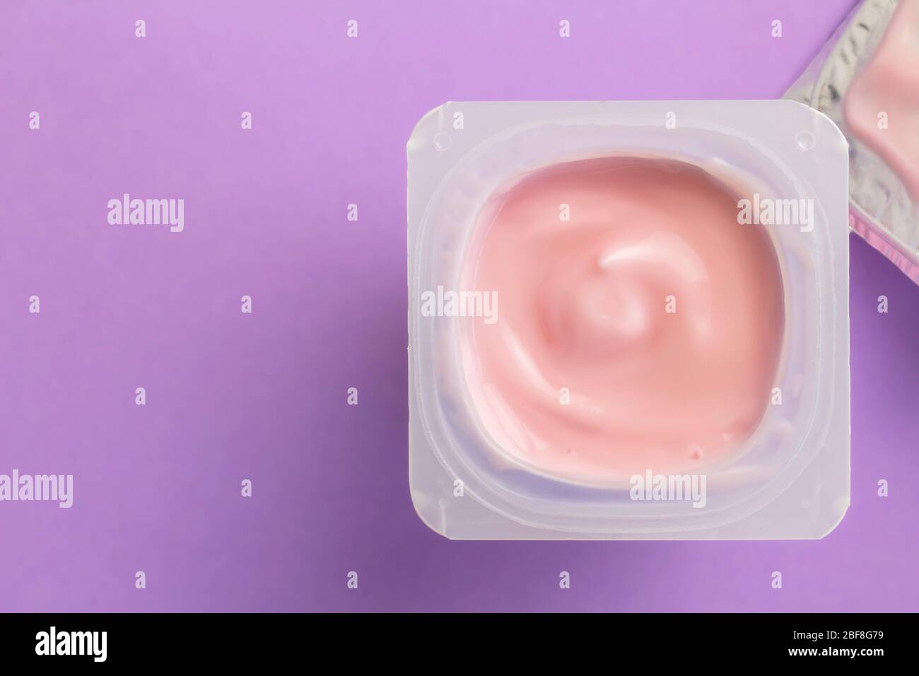 Tazza di yogurt con yogurt alla fragola isolata su sfondo lilla con spazio per il testo Foto Stock