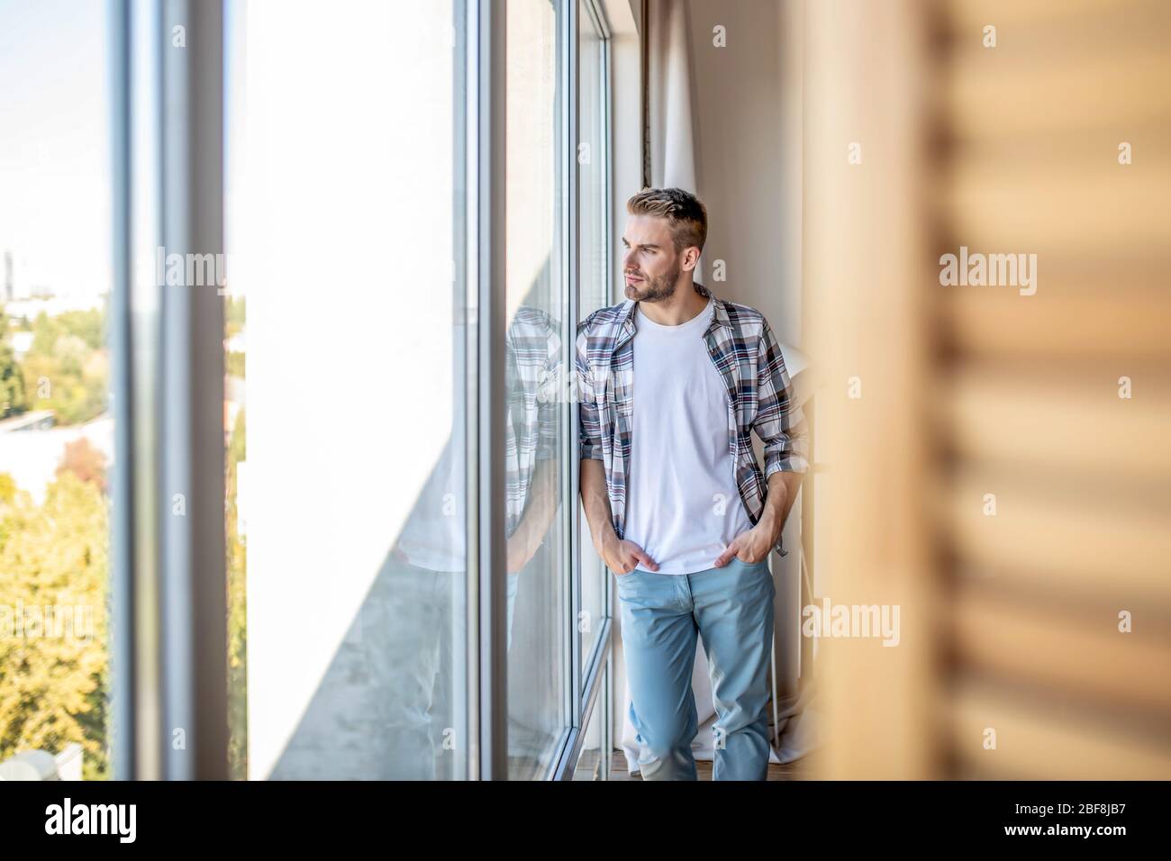 Giovane uomo in camicia a scacchi che guarda fuori dalla finestra Foto Stock
