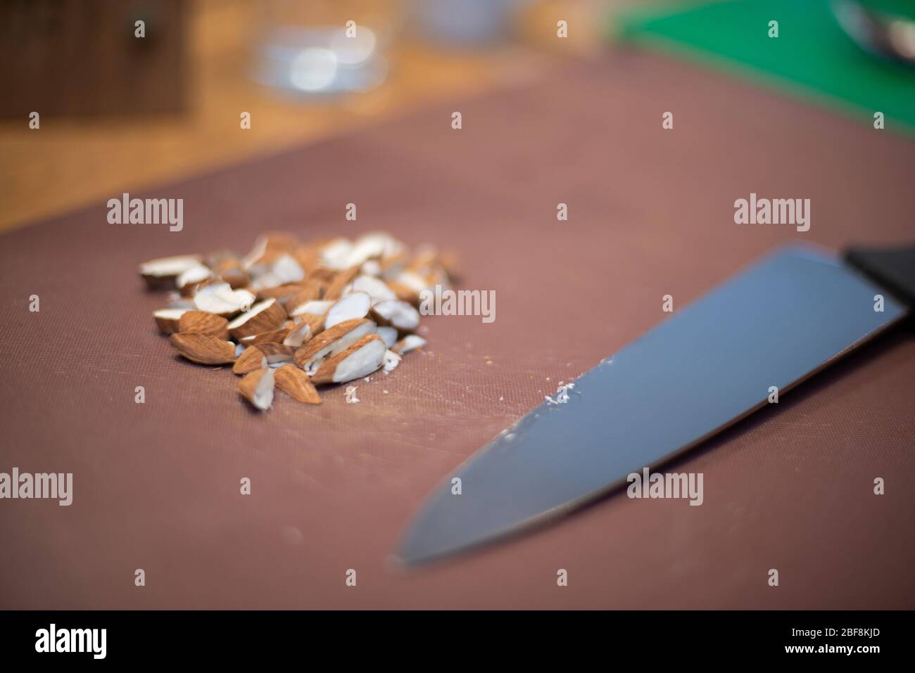 Una manciata di mandorle, appena tritate, giacciono su un tagliere accanto a un coltello in acciaio inossidabile all'interno di una cucina Foto Stock