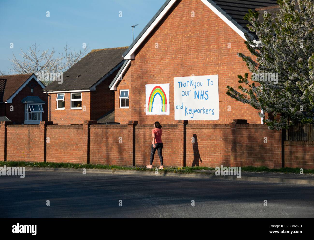 Lady Runner passeggiando davanti a un NHS e Keyworkers grazie banner. Anche con un arcobaleno dipinto su casa, in mezzo al coronavirus di blocco nel Regno Unito Foto Stock