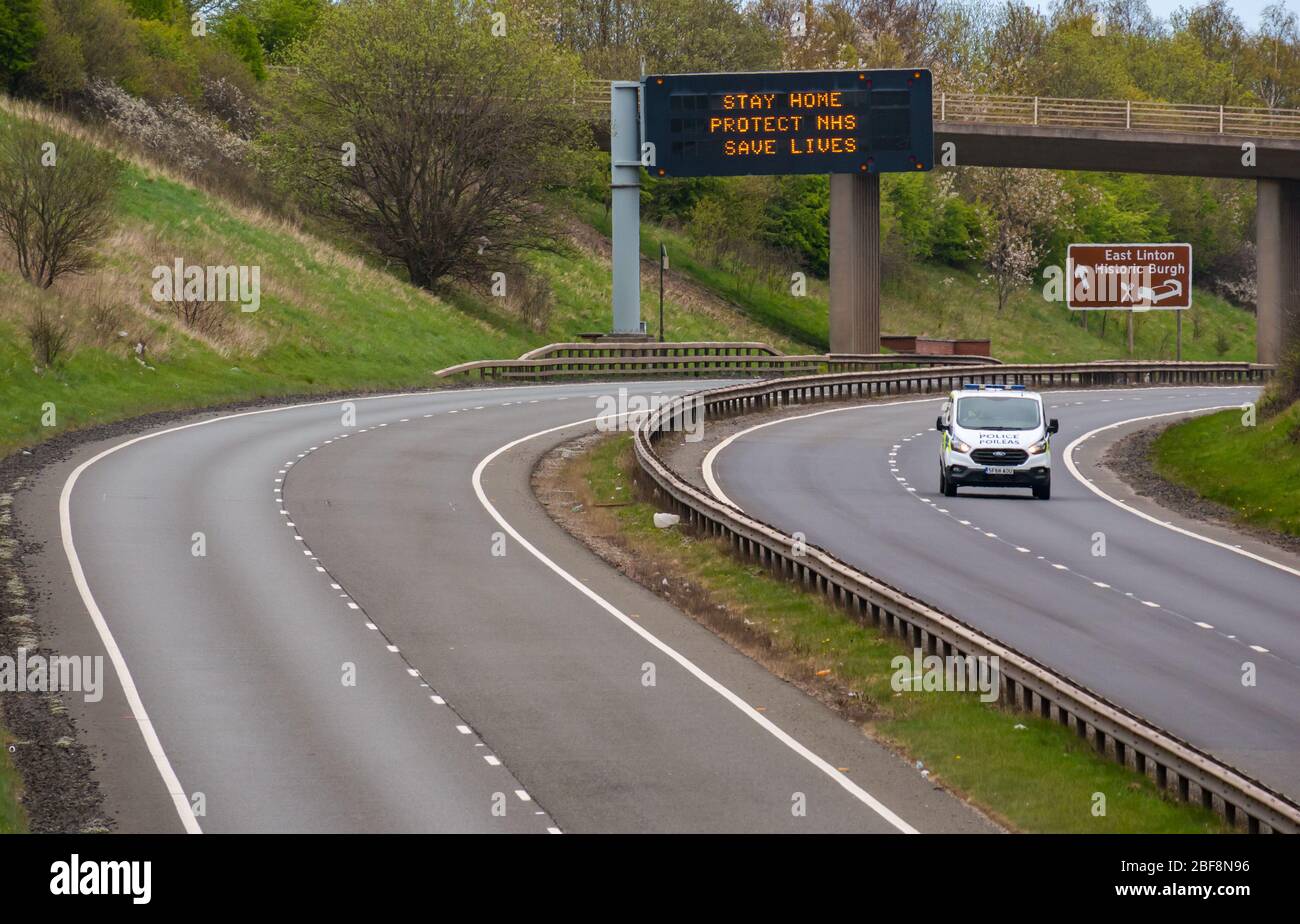 East Lothian, Scozia, Regno Unito, 17 aprile 2020. Covid-19 Lockdown su A1: Come il paese entra nella seconda fase dell'annunciata estensione delle misure di blocco, la normale A1 a doppia carreggiata che collega la Scozia con l'Inghilterra è quasi deserta con pochissimo traffico oltre a quelli su viaggio essenziale come un veicolo di polizia. Un gantry sospeso ha il messaggio pandemico rimanere sicuri, proteggere NHS, salvare vite Foto Stock