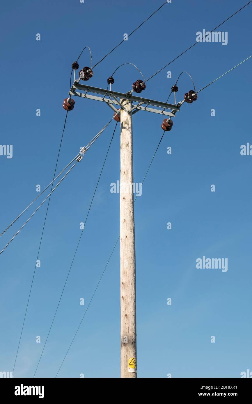 Un polo elettrico in legno ad alta tensione con isolatori in ceramica visti contro un cielo blu, nella campagna del Regno Unito Foto Stock