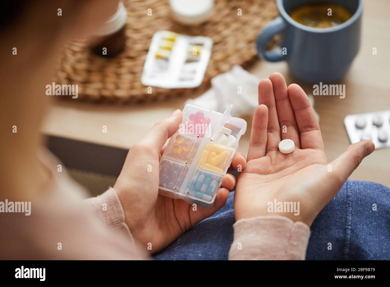 Primo piano della donna che tiene la scatola con le compresse e lei sta andando bere quello da mal di testa mentre siede a casa Foto Stock