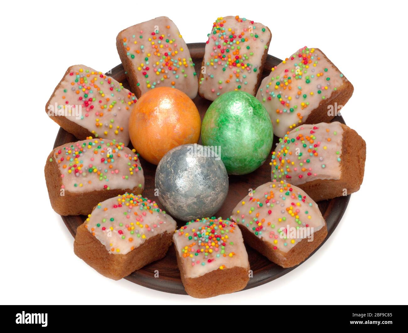 Mini torte pasquali con glassa e spolverine di zucchero colorate e tre uova colorate in un piatto Foto Stock