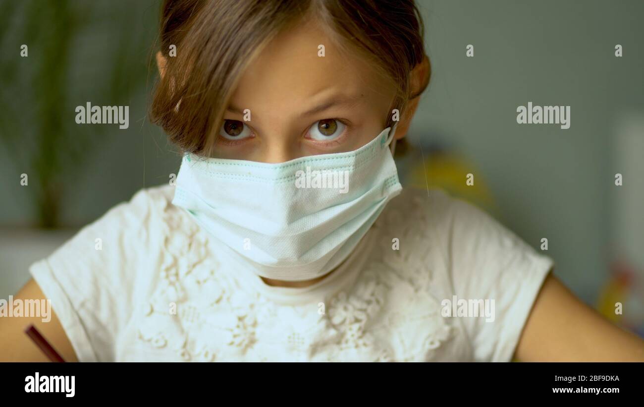 Formazione a domicilio durante il periodo di quarantena del Coronavirus Covid19. Una ragazza in una maschera medica protettiva fare i compiti. Vista ravvicinata. Foto Stock