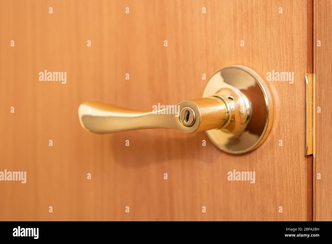 Maniglia inclinata in colore oro sullo sfondo di una porta in legno. Elemento della porta Foto Stock
