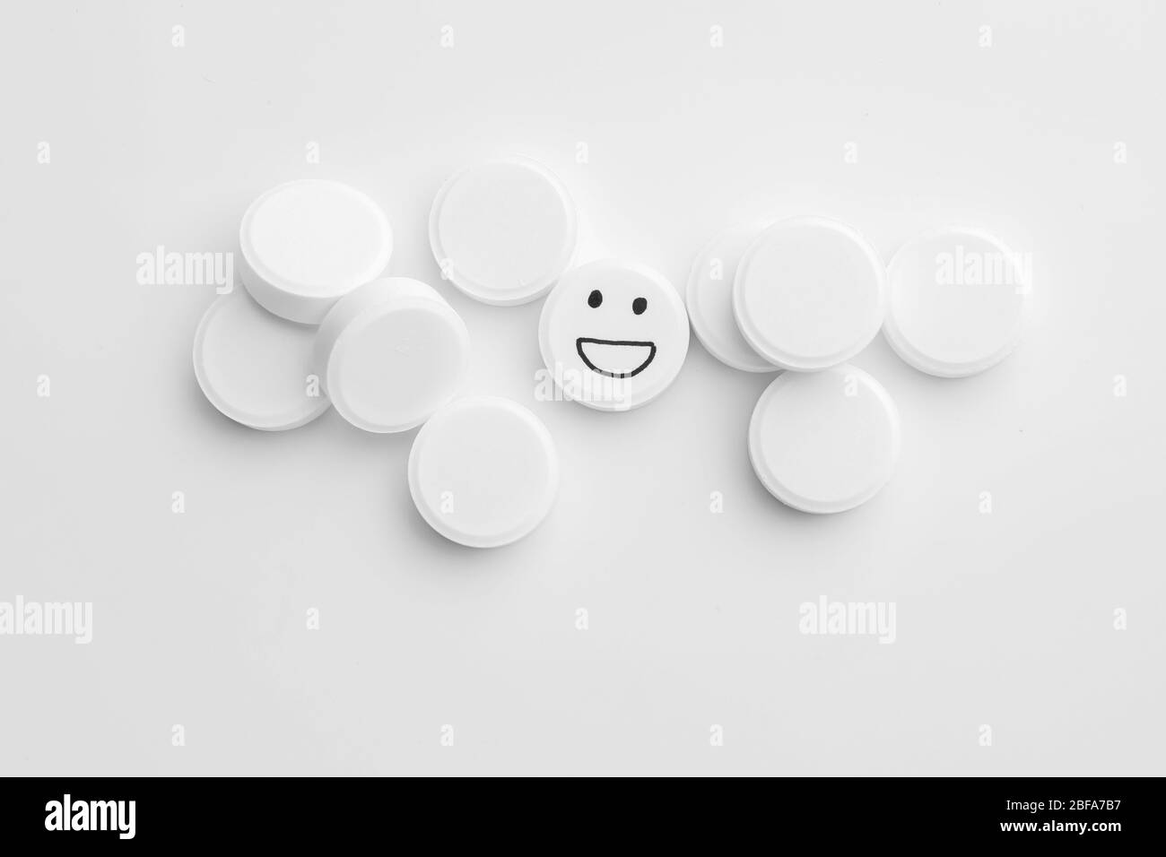 Una pillola con faccia felice disegnata tra quelle bianche, vista dall'alto Foto Stock