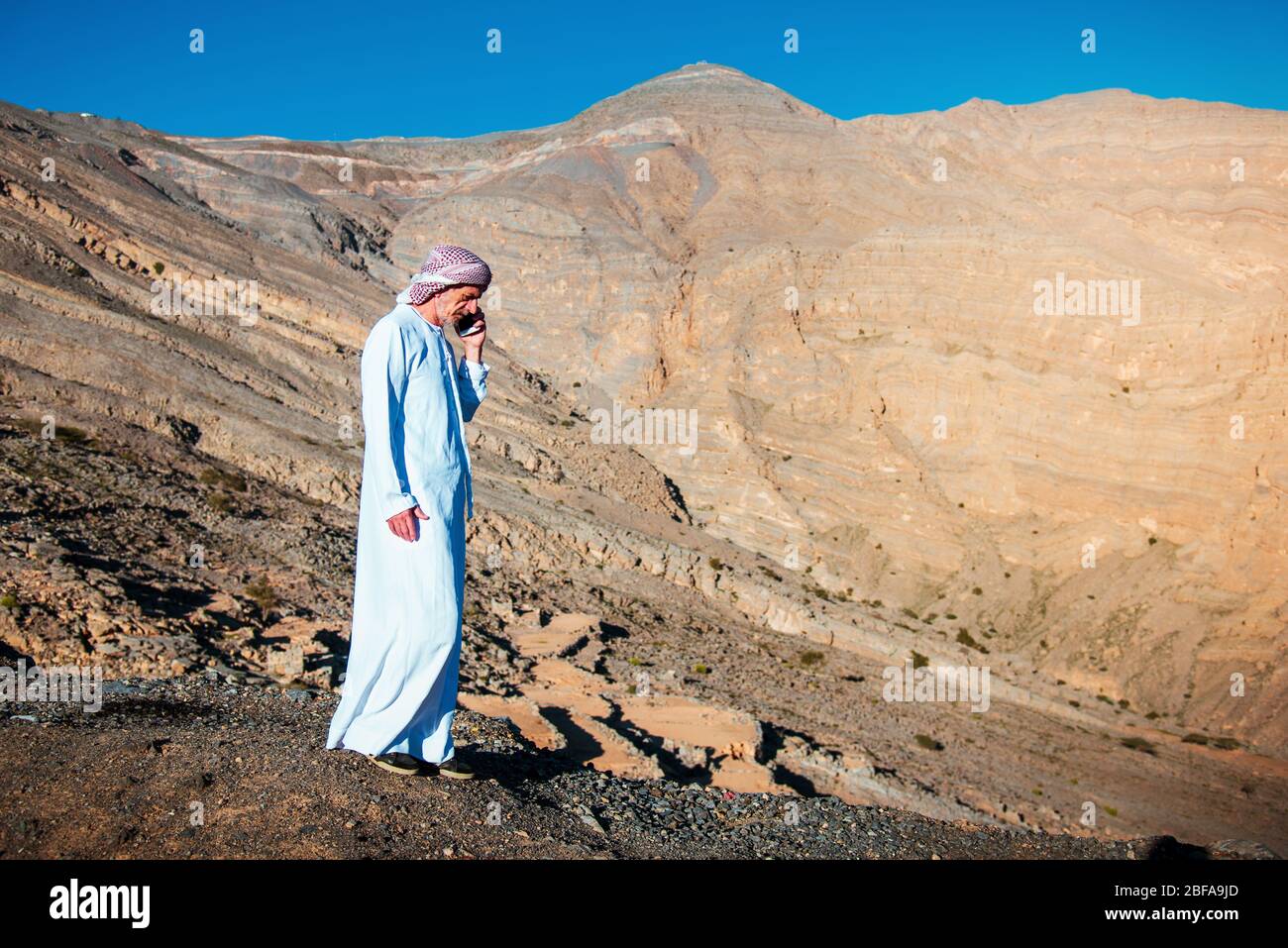 Uomo arabo che usa il telefono con arenaria montagna sfondo superiore degli Emirati Arabi Uniti Foto Stock
