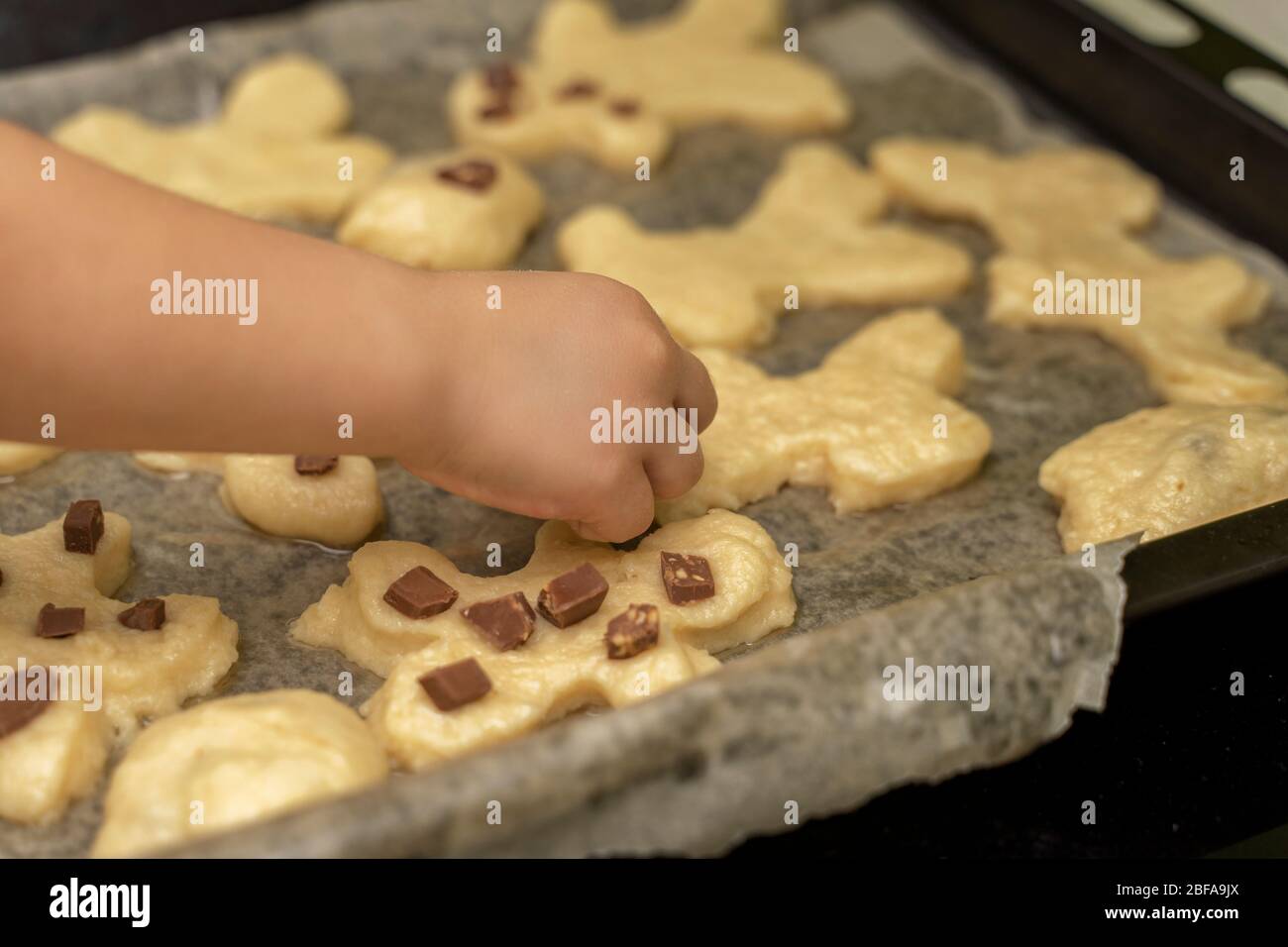 la mano di un bambino decora pezzi di cioccolato con biscotti fatti in casa su una teglia. attività con i bambini nel periodo di quarantena a casa Foto Stock