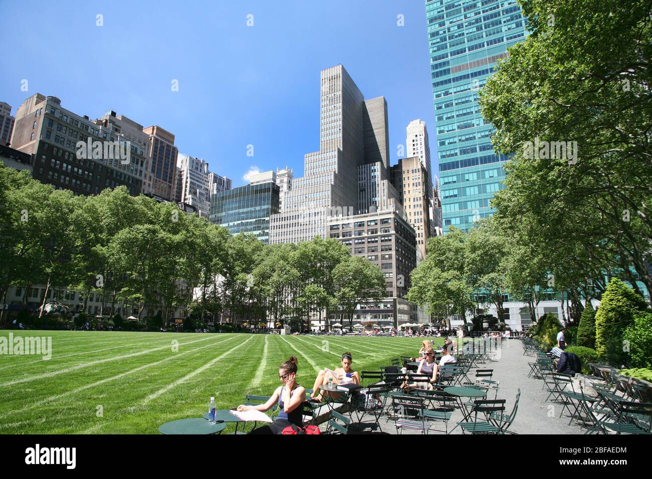 Persone che si rilassano in una splendida giornata estiva primaverile al Bryant Park, a Midtown Manhattan, in 42nd Street tra la 5th e 6th Avenue a New York City, USA Foto Stock