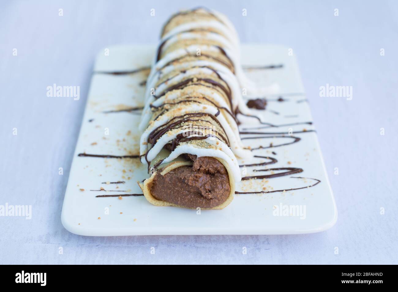 Una frittella con farcitura di cacao, ricoperta di panna montata, decorata con cioccolato fuso e cosparse di biscotti macinati. Foto Stock