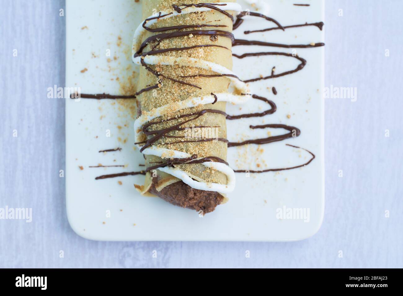 Pancake europeo o palatschinke o palacinka con farcitura di cacao e crosta a mollo, decorata con farcitura al cioccolato, panna montata e biscotti macinati. Foto Stock