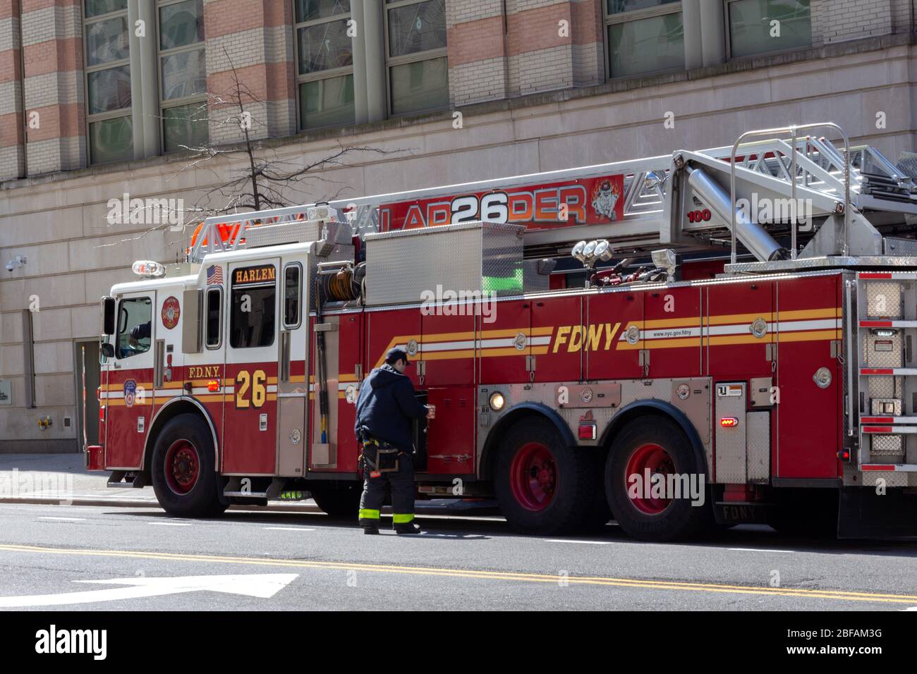 un vigile del fuoco accanto a un camion per motori antincendio. Legge la scala 26 Harlem, parte del Dipartimento dei Vigili del fuoco di New York o FDNY Foto Stock