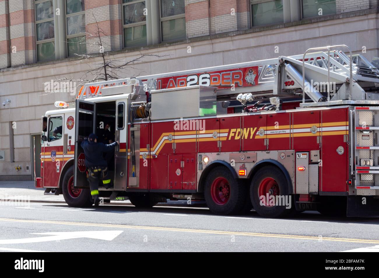un vigile del fuoco accanto a un camion per motori antincendio. Legge la scala 26 Harlem, parte del Dipartimento dei Vigili del fuoco di New York o FDNY Foto Stock