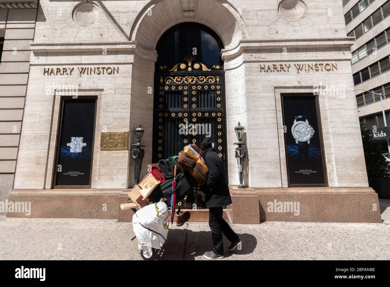 Un uomo senza tetto che spinge il suo carrello degli effetti personali si gira per guardare il deposito di gioielli di Harry Winston sulla Fifth Avenue, un'immagine potente della disuguaglianza di reddito Foto Stock