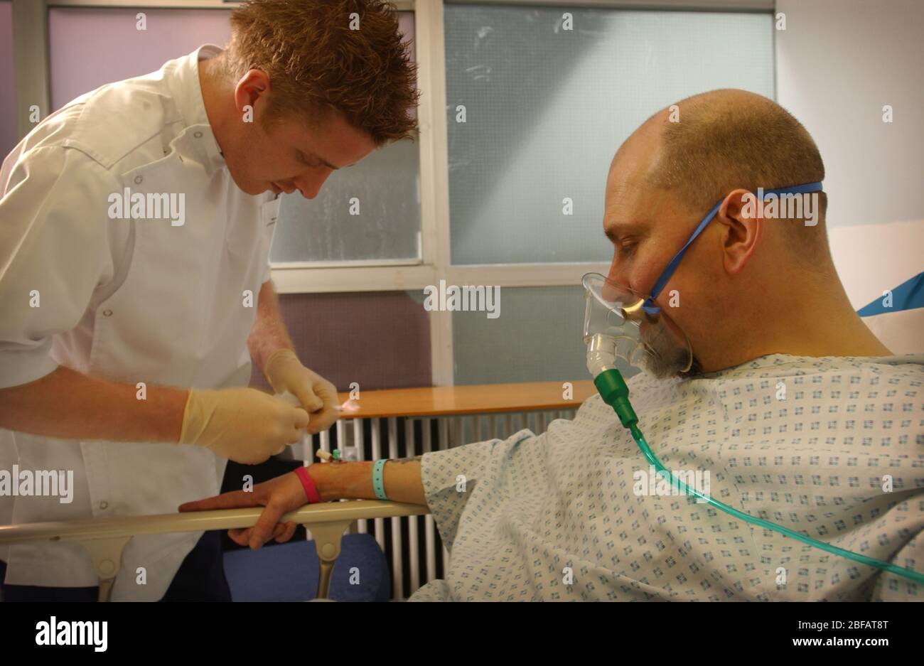L'infermiere maschio inserisce una gocciolamento endovenoso nel braccio di un paziente che indossa una maschera per l'ossigeno Foto Stock