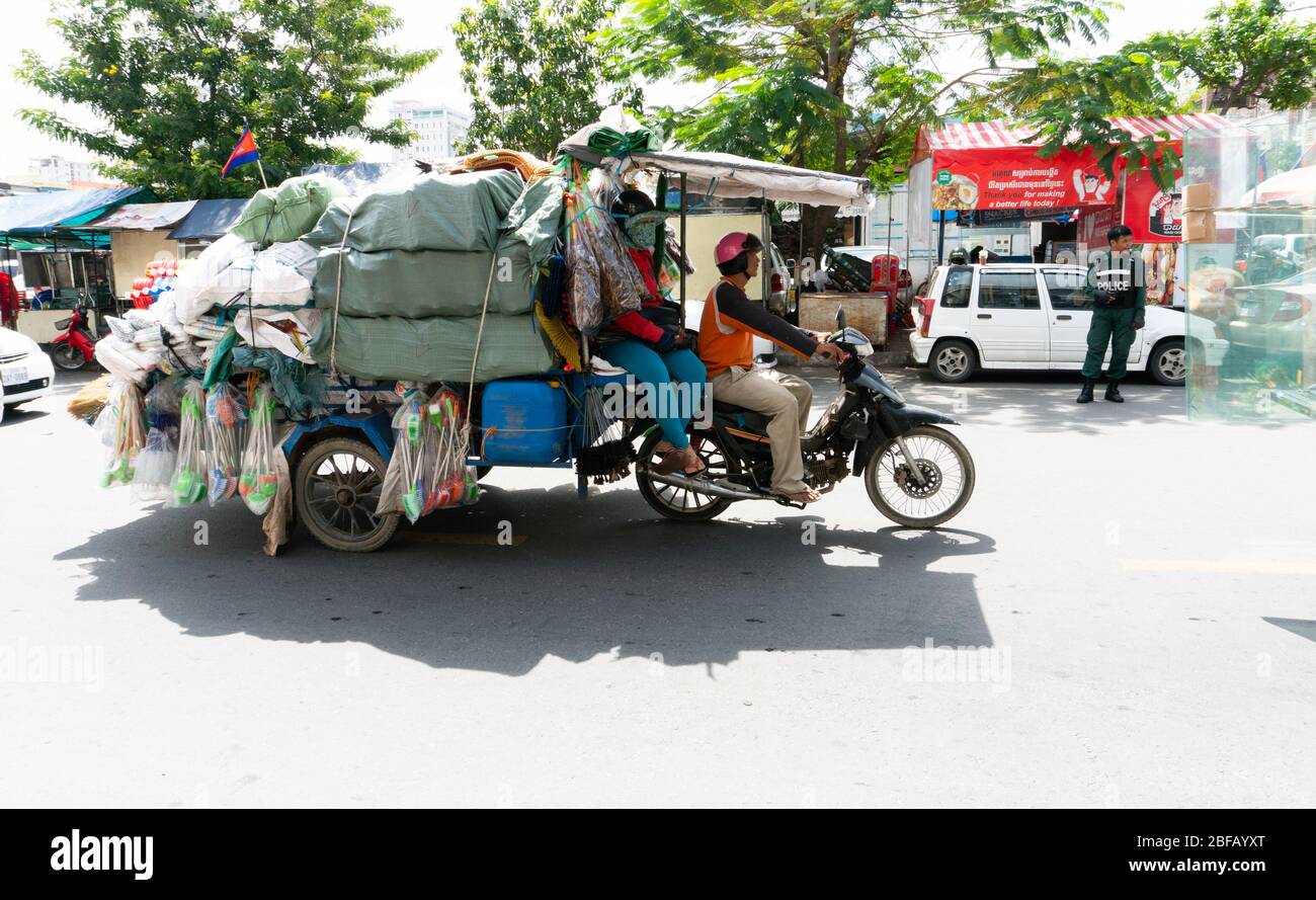 Phnom Penh, Cambogia - Giugno 25,2018: street scene con due venditori di strada su una moto con un sacco di merci. Foto Stock