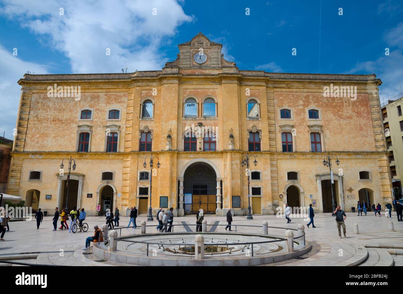 Matera, Italia - 6 maggio 2018: Persone a piedi vicino al Cinema Comunale Palazzo dell'Annunziata con orologio sulla facciata e fontana su Piazza Vittorio V. Foto Stock