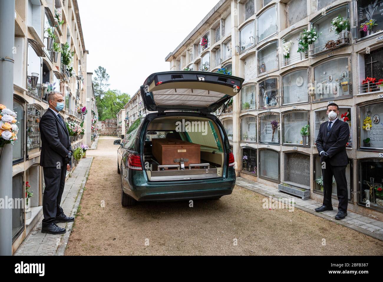 I lavoratori funebri si trovano accanto a un veicolo funerale durante un funerale. Il Covid-19 rende i funerali difficili, la situazione richiede ai lavoratori di indossare maschere e sono costretti a limitare l'accesso, in alcuni casi le cerimonie sono senza membri della famiglia. Foto Stock