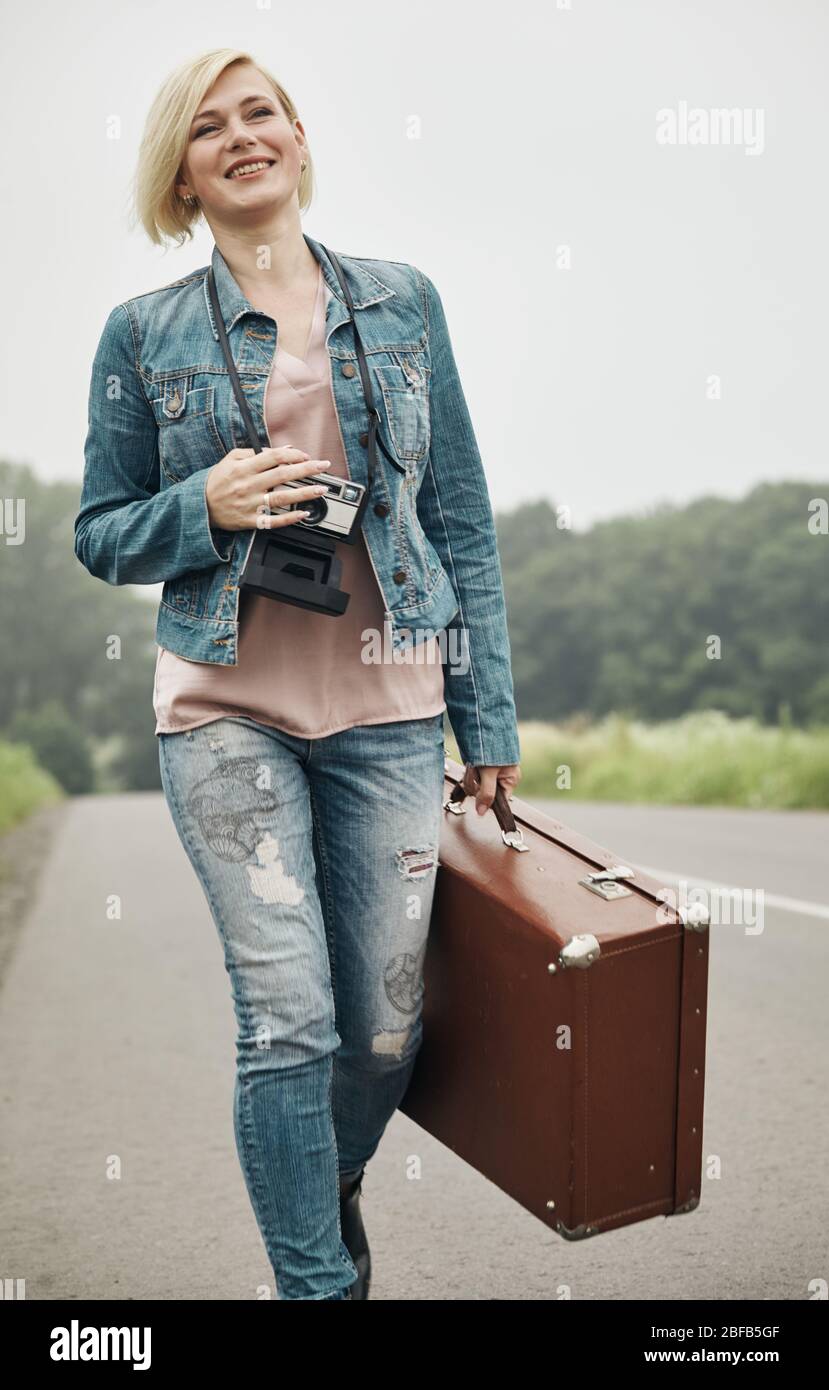 Traveler ragazza con una valigia sulla strada. Concetto di viaggi, vacanze, solo-turismo femminile, viaggi avventura. Foto Stock