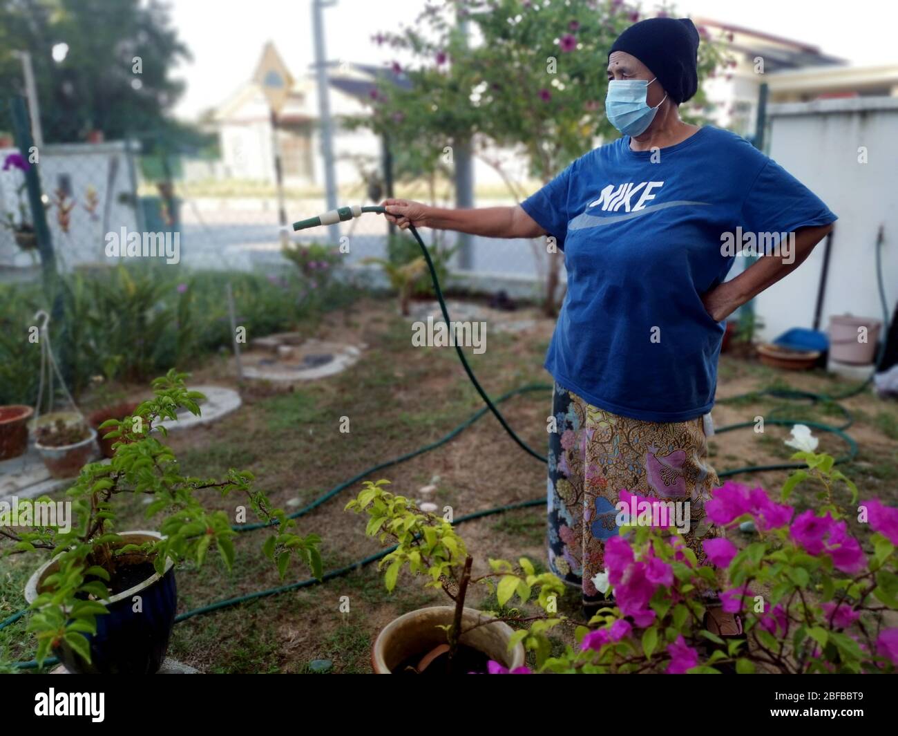 Donne asiatiche che annaffiano il fiore indossando maschera perché corona virus pandemico in tutto il mondo Foto Stock