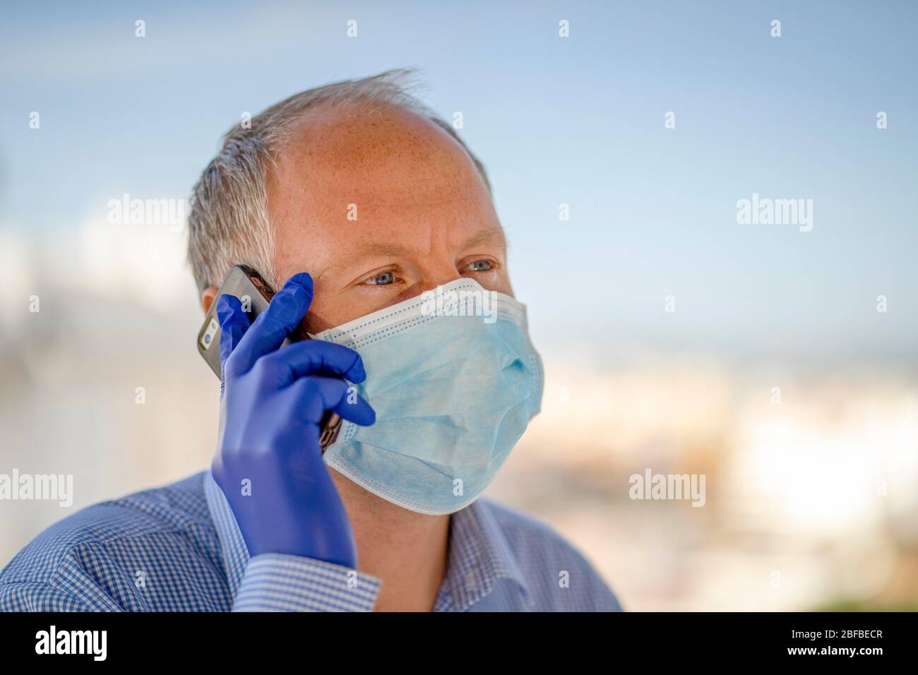 Uomo con maschera protettiva e guanti in lattice blu mentre si utilizza il telefono cellulare, Germania Foto Stock