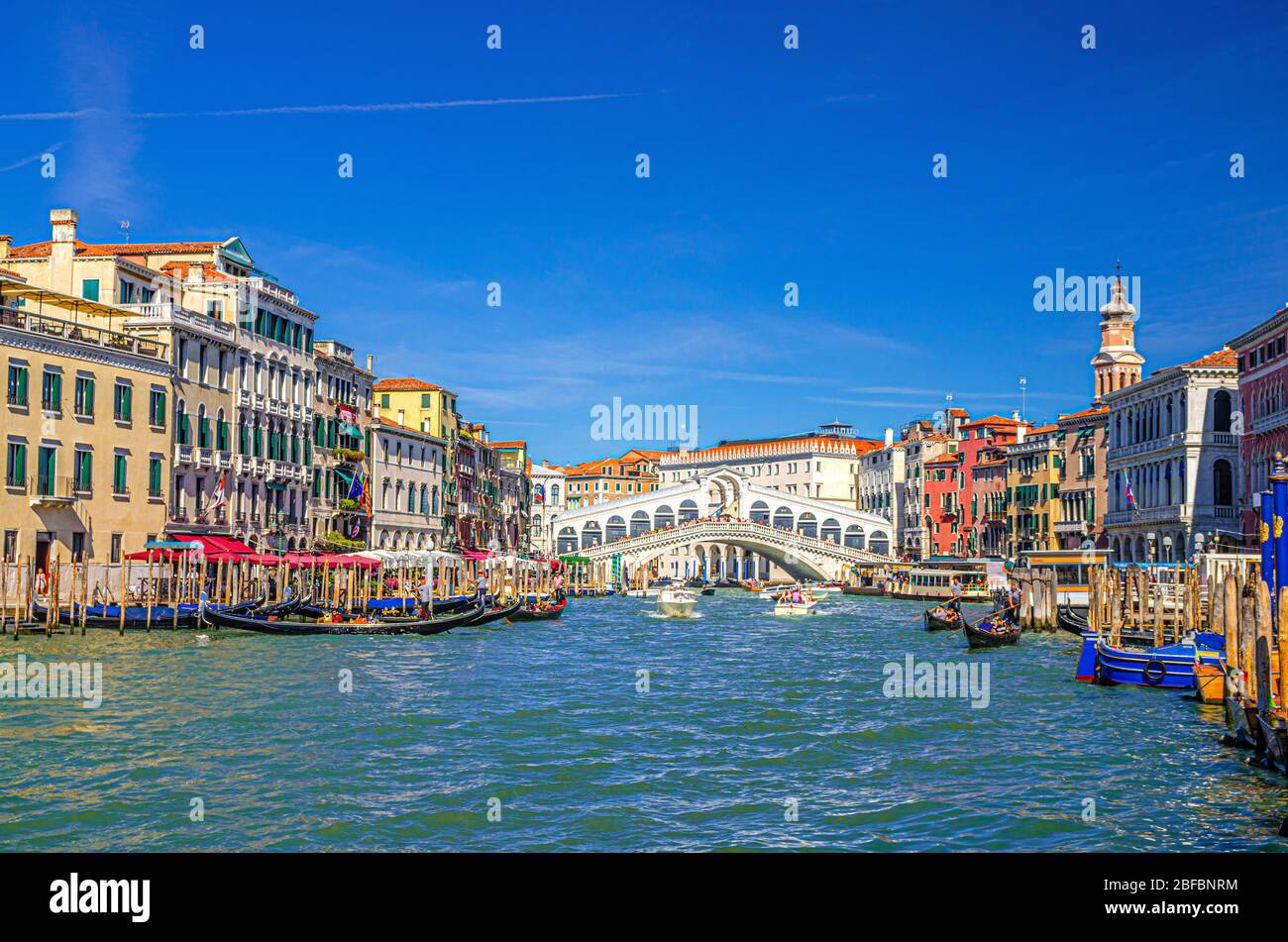 Venezia con il Ponte di Rialto attraverso il canale navigabile del Canal Grande, architettura veneziana edifici colorati, gondole, barche, vaporetti ormeggiati e veleggiati Foto Stock