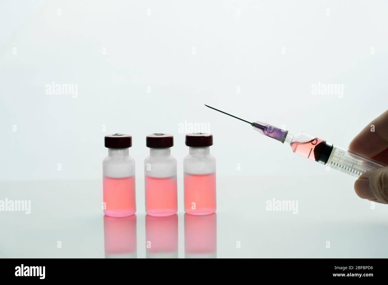 siringa per tenere le mani e farmaco rosso in flacone per il trattamento di malattie mediche su fondo bianco clinico Foto Stock