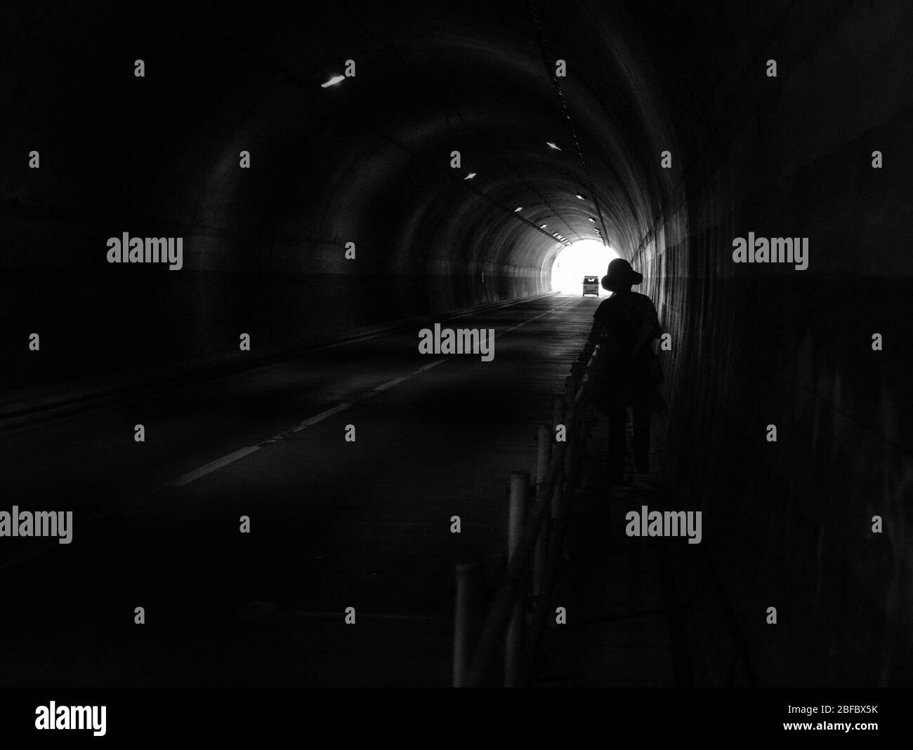 Silhouette umana e automobilistica nel tunnel scuro. Luce alla fine del tunnel. Foto Stock