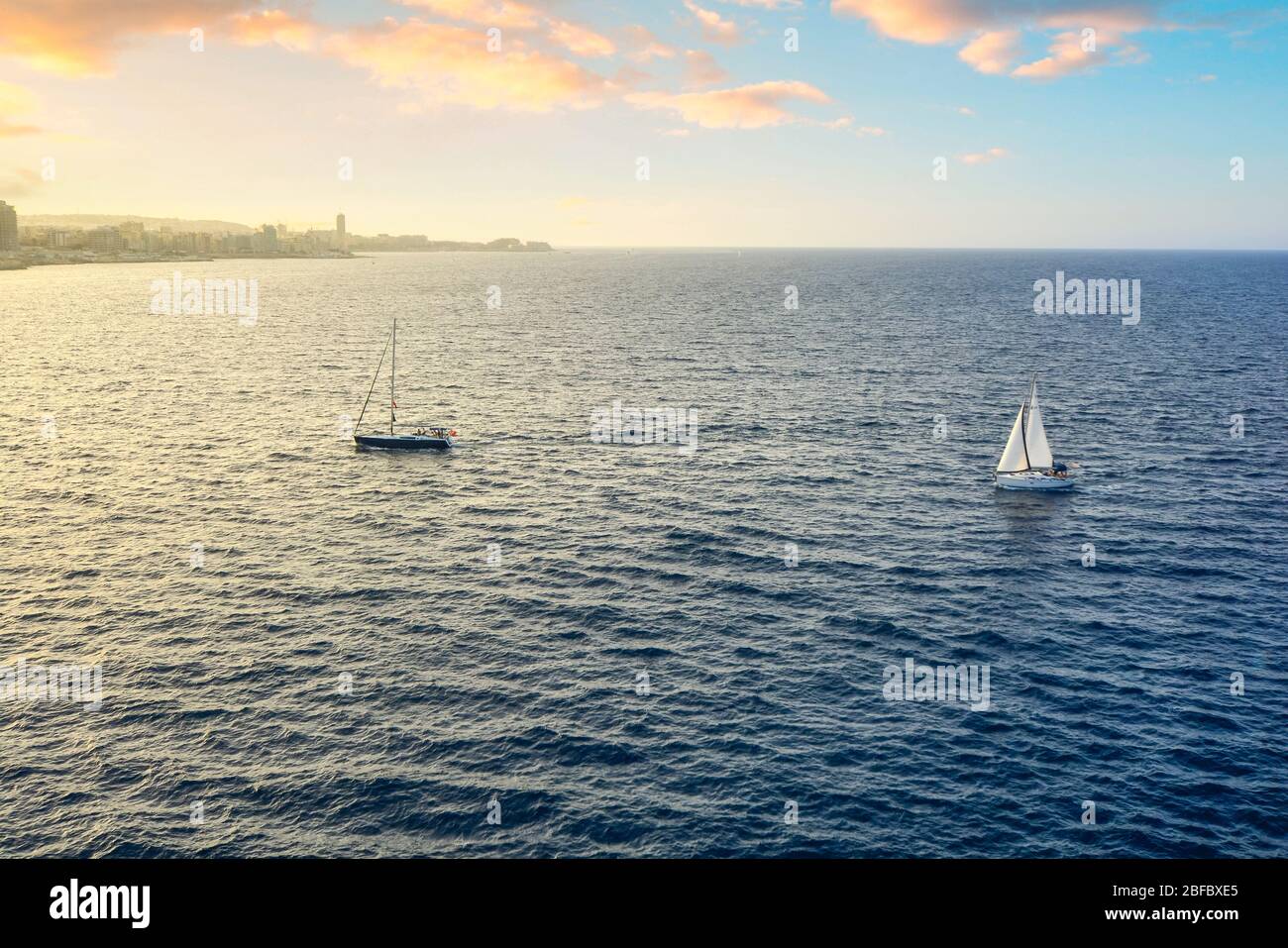 Due barche a vela appena fuori dal porto e le mura della città antica di la Valletta Malta, e l'isola nel Mar Mediterraneo. Foto Stock