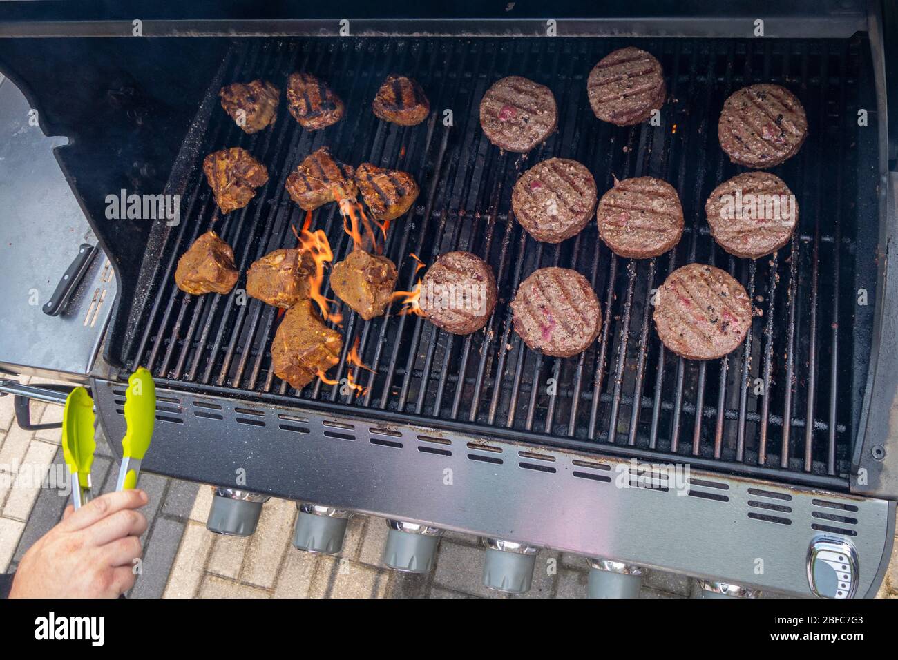 Uomo che cucina hamburger di manzo e costolette di agnello barbecue su una griglia esterna di gas propano estate Foto Stock
