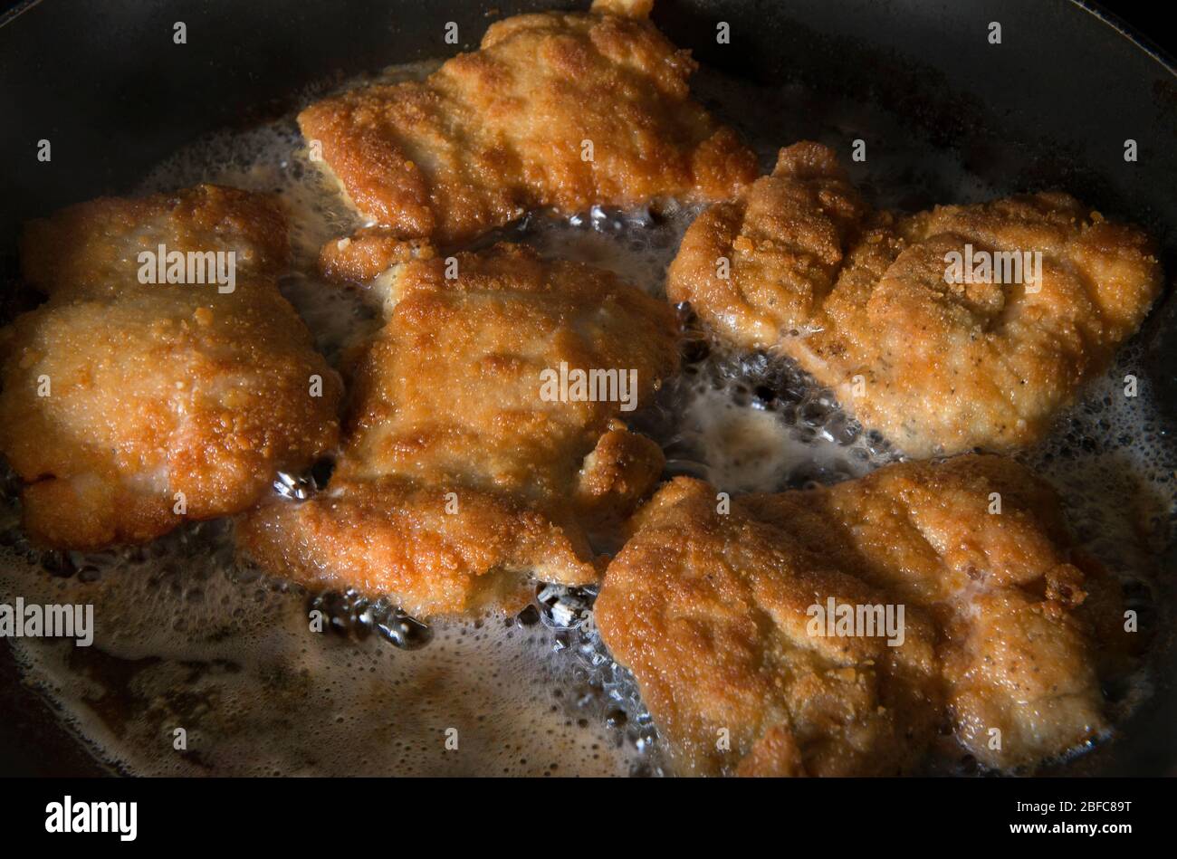 Coscia di pollo impanata disossata in una padella con olio vegetale caldo, una procedura per friggere e preparare il cibo in olio Foto Stock